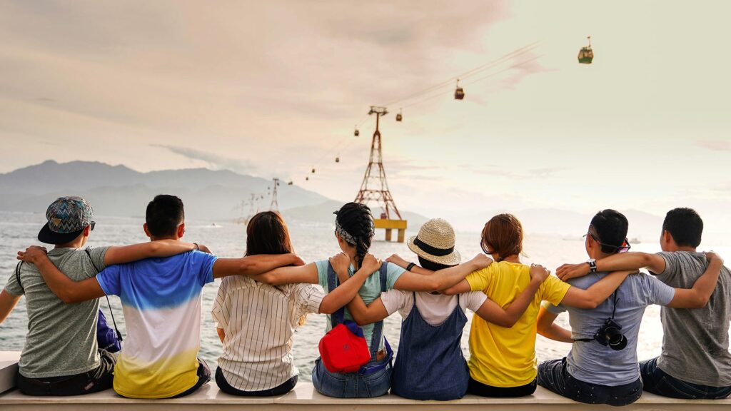 Group of solo travelers sitting together with arms around each other, enjoying a scenic view of the ocean and cable cars.