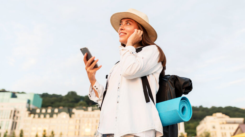 Smiling woman with a backpack and phone, enjoying a solo travel experience in a city with scenic buildings in the background.