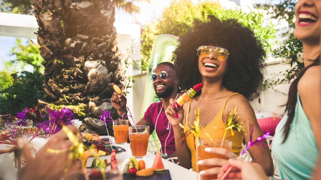 Friends enjoying a vibrant Juneteenth celebration outdoors, laughing and sharing fruit and drinks at a sunny summer gathering.