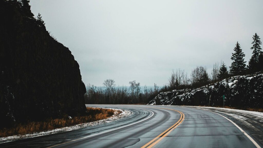A winding stretch of North Shore Drive in Minnesota curves through snow-dusted cliffs and bare winter trees under a gray sky, highlighting a peaceful and scenic road trip in the USA.