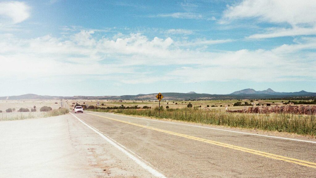 A white car cruising along the historic Route 66 highway, surrounded by open plains and distant mountains, symbolizing the freedom of road trips in USA.