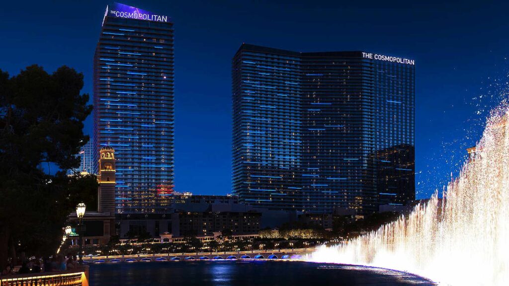 The Cosmopolitan of Las Vegas illuminated at night beside the Bellagio fountains, showcasing one of the most iconic luxury hotels in Las Vegas with upscale accommodations and nightlife.