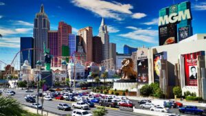 Daytime view of the Las Vegas Strip featuring iconic luxury hotels including MGM Grand and New York-New York, with the replica Statue of Liberty, roller coaster, and vibrant cityscape.