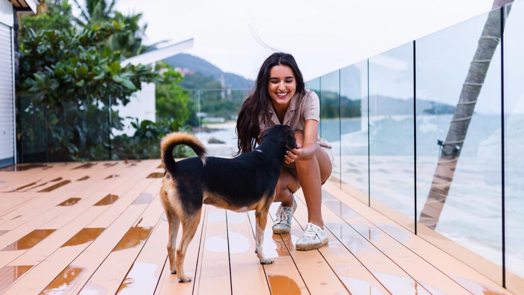 A smiling woman petting her dog on the deck of a beachside resort, highlighting the welcoming atmosphere of pet-friendly hotels for coastal getaways.