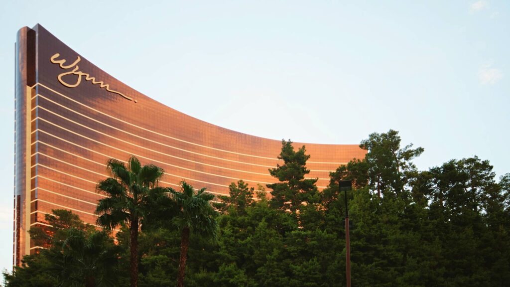 The sleek curved facade of Wynn Las Vegas rising above lush greenery, representing one of the top luxury hotels in Las Vegas for upscale stays and scenic surroundings.
