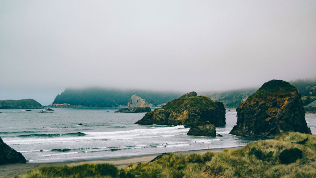Dramatic coastal view of Cannon Beach, Oregon, featuring rugged sea stacks, misty hills, and gentle waves—an ideal destination for affordable beach vacations in the Pacific Northwest.