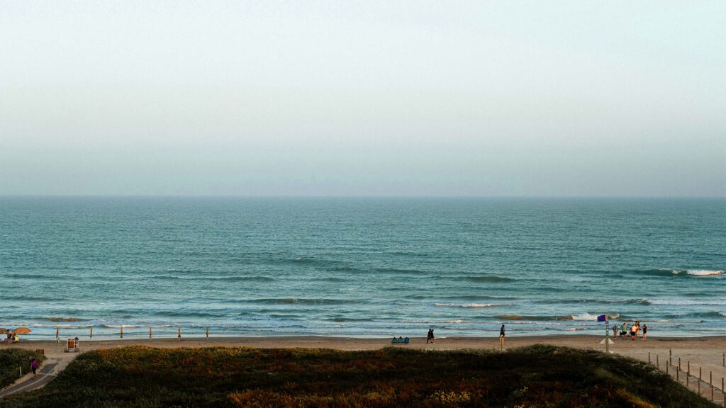 A calm beach at South Padre Island, Texas, with gentle waves, a few people walking, and beach chairs near the shore—an ideal spot for affordable beach vacations with peaceful views and budget-friendly coastal charm.