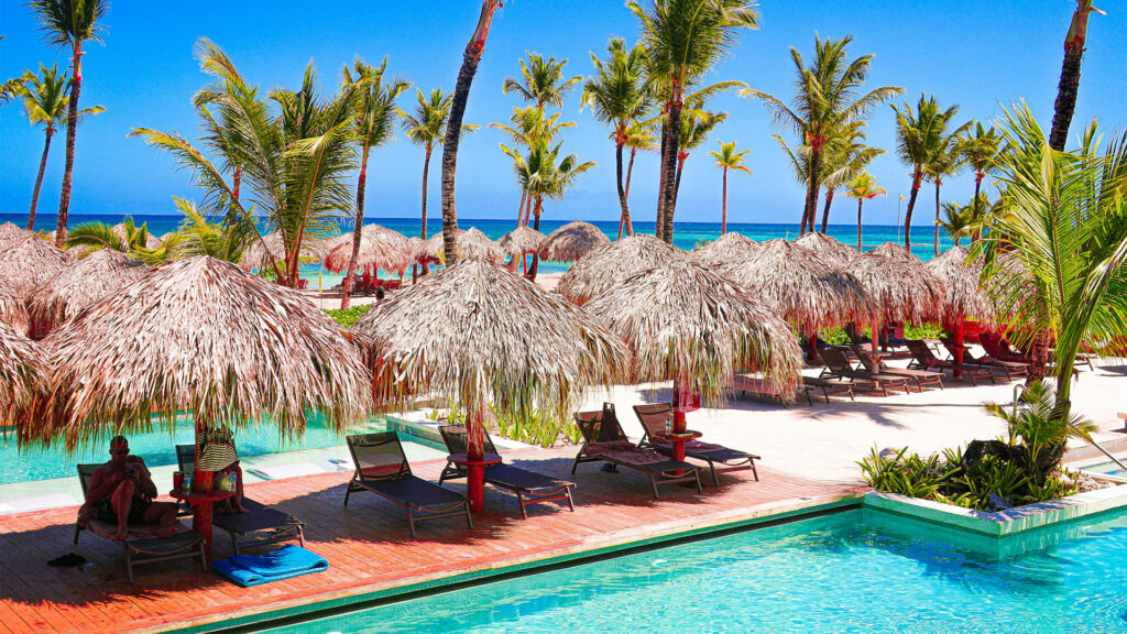 Thatched-roof cabanas and palm trees beside a luxury pool at Punta Cana all inclusive resorts