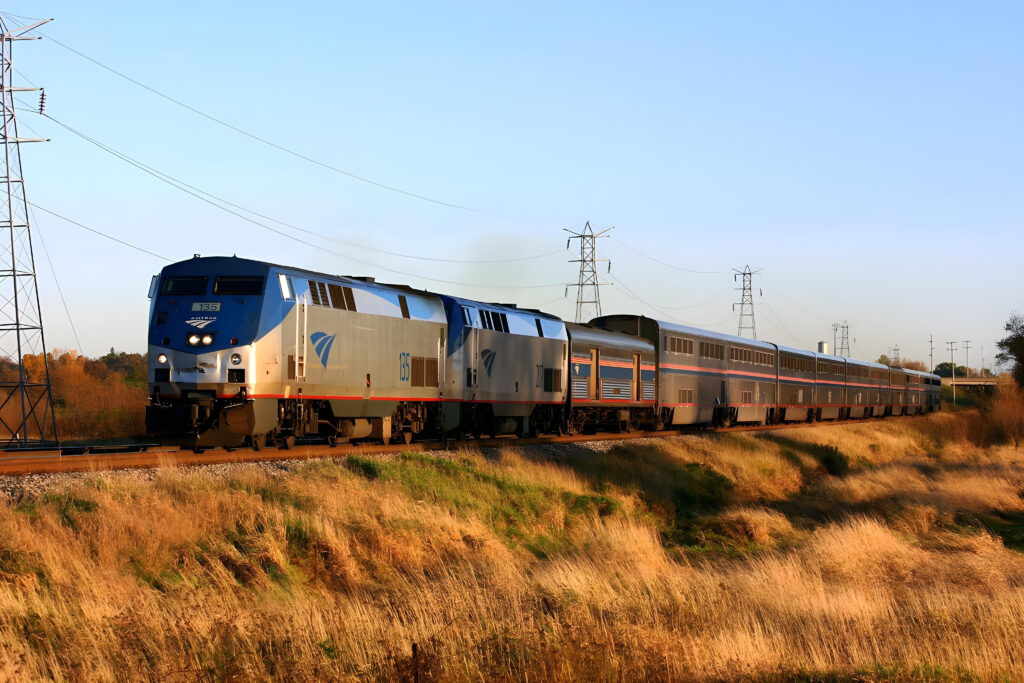 Amtrak Empire Builder train with dual locomotives and bi-level Superliner coaches moving through open fields under a clear sky.