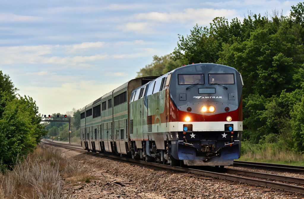 Amtrak train painted in a patriotic red, white, and blue scheme traveling through forested countryside.
