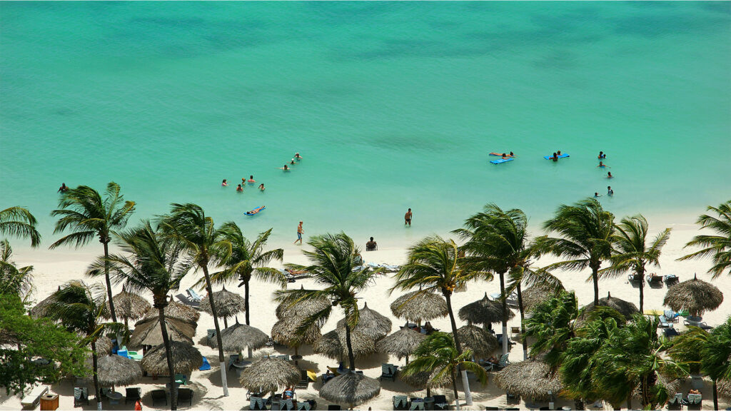 Tourists enjoying the turquoise waters and sandy beach in Aruba, part of all inclusive trips.