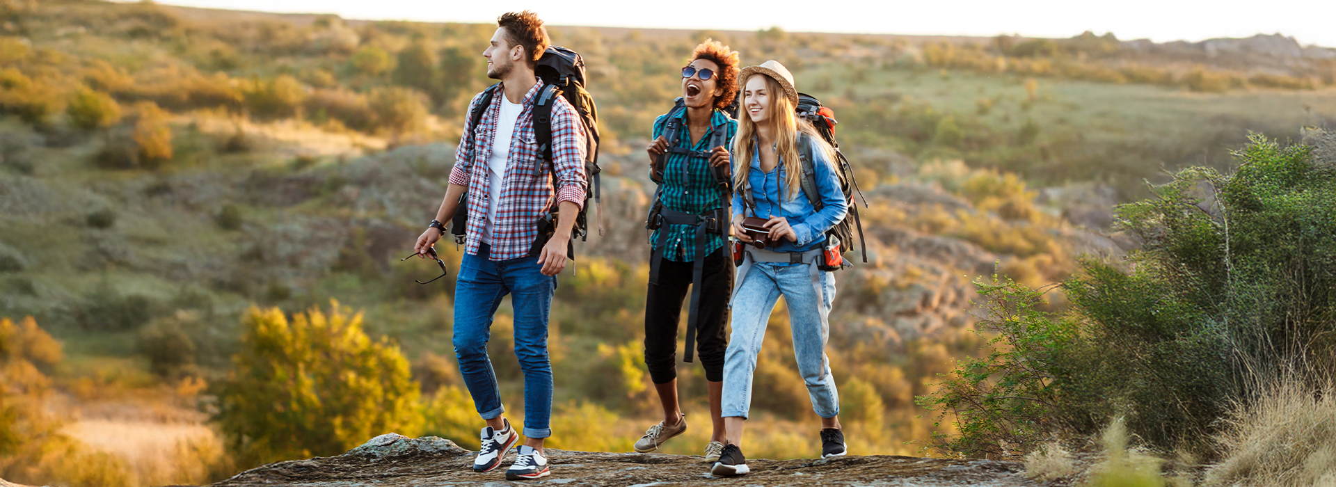 Group of three young people hiking in nature with backpacks, smiling and enjoying their adventure.