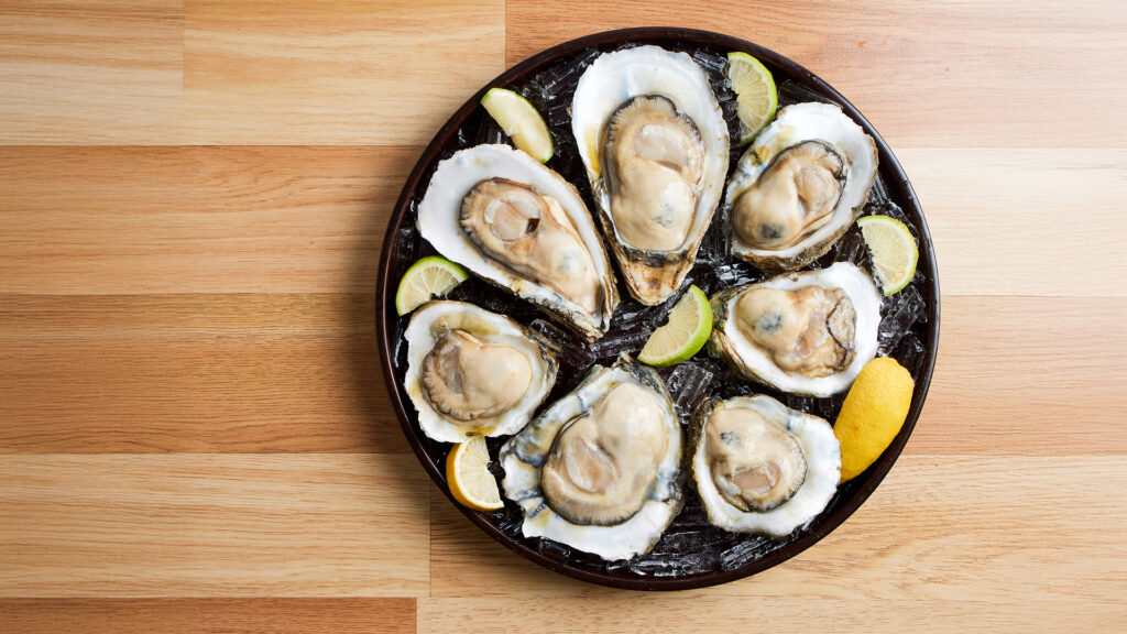 A plate of fresh oysters served on ice with lemon and lime wedges.