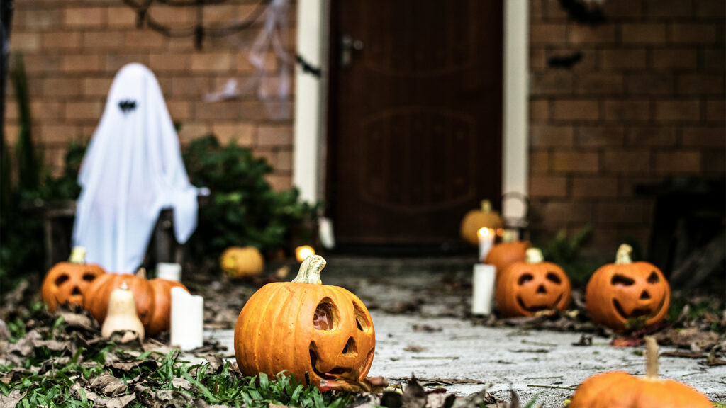 A ghostly figure and carved pumpkins lining the path in front of a house, creating a spooky Halloween atmosphere.
