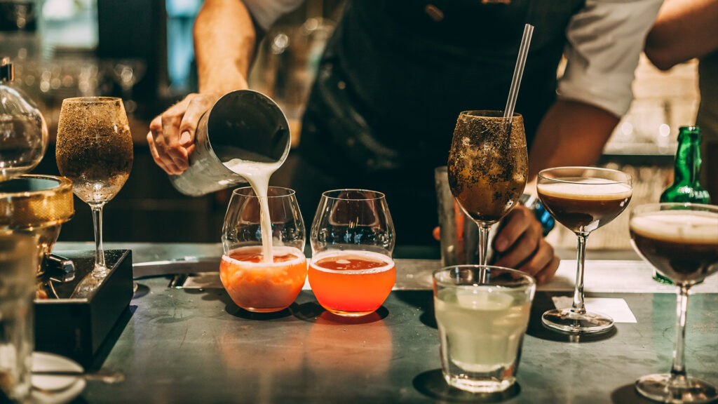 A bartender pouring milk into colorful cocktails at a bar. Stay in nearby Los Angeles hotels to experience the city's thriving nightlife and bars.