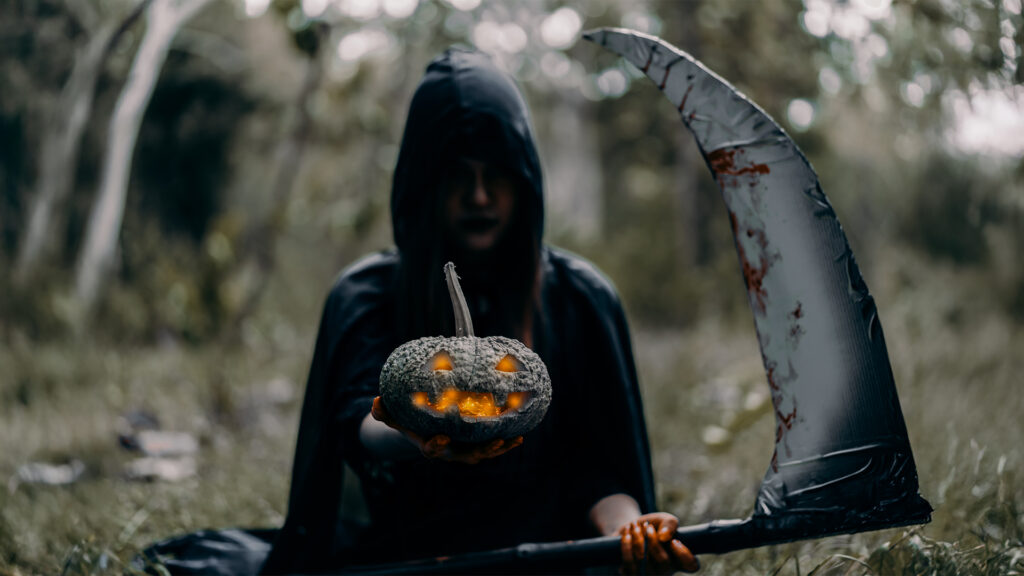 A spooky Halloween scene with a figure in a dark hood holding a carved pumpkin, set against an eerie forest backdrop.