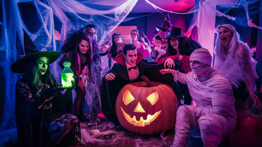 A vibrant Halloween party with guests in costumes, including a vampire, witch, and mummy, gathered around a glowing pumpkin.