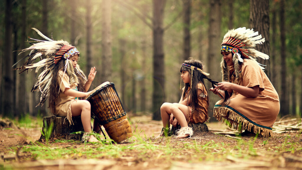 Playing the song of their people shot of a young woman and her two daughters playing dressup in the woods