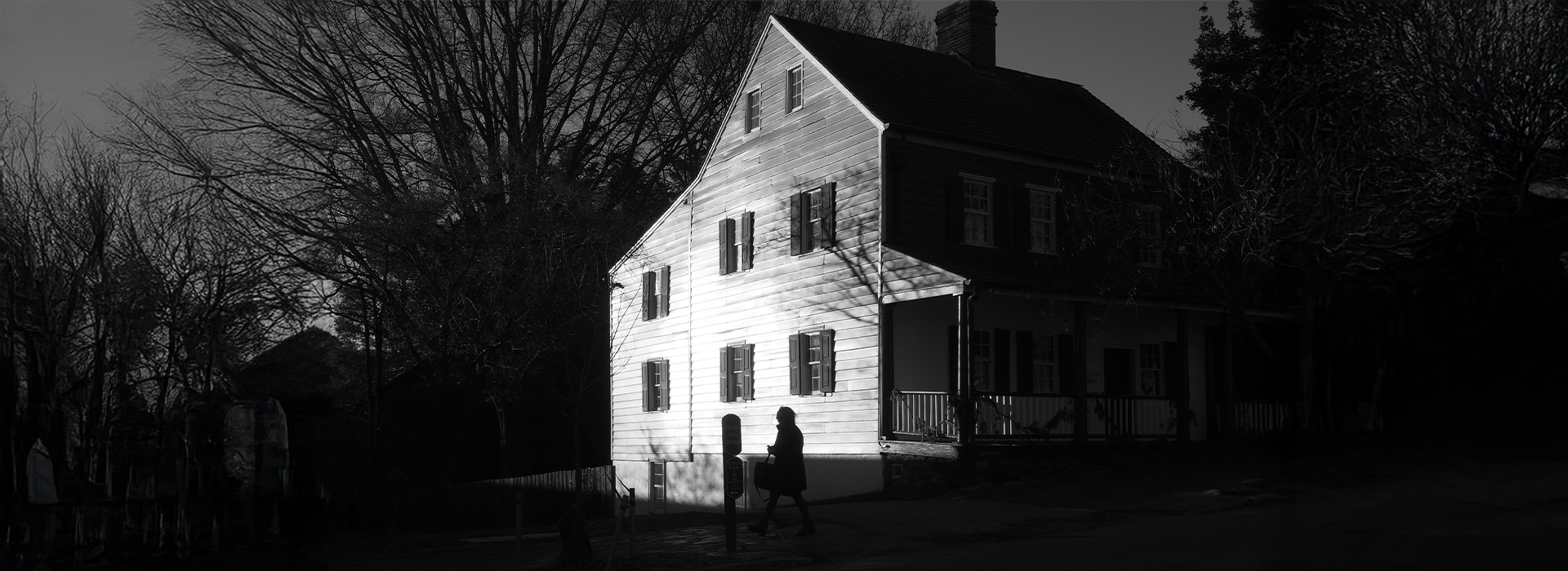 A spooky, dimly lit house with shadows cast by bare trees, evoking a haunting atmosphere, making it one of the eerie spots in America.