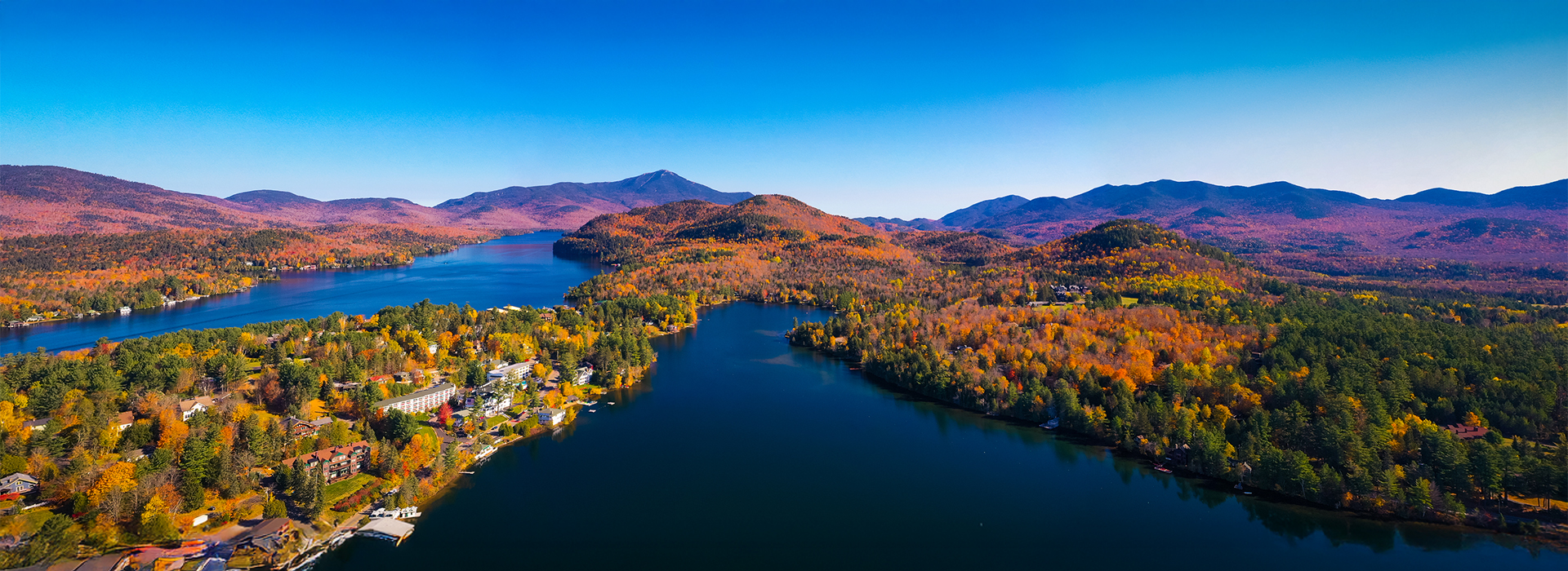 Aerial view of a lake surrounded by colorful fall foliage and mountains in the Adirondacks, New York.