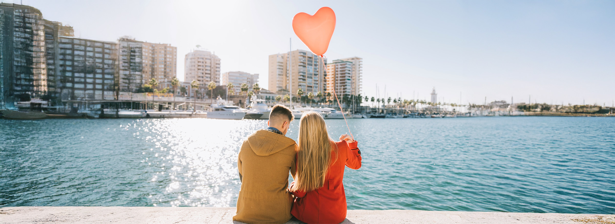 A couple sitting by the waterfront, enjoying a romantic moment with a heart-shaped balloon — perfect for a couple's getaway.