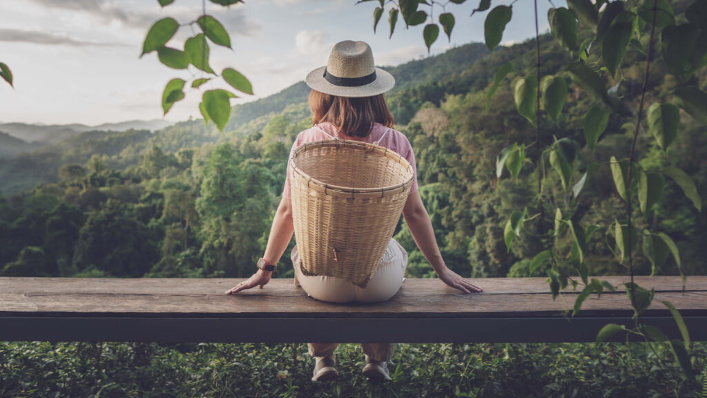 Traveler enjoying a peaceful moment in nature, sitting with a basket on a wooden bench – Sustainable Travel Tips for eco-conscious explorers.