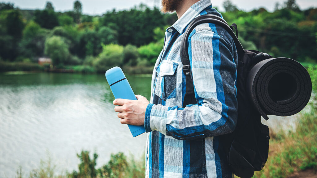 Traveler carrying a reusable bottle and backpack near a lake – Sustainable Travel Tips for reducing plastic waste on trips.