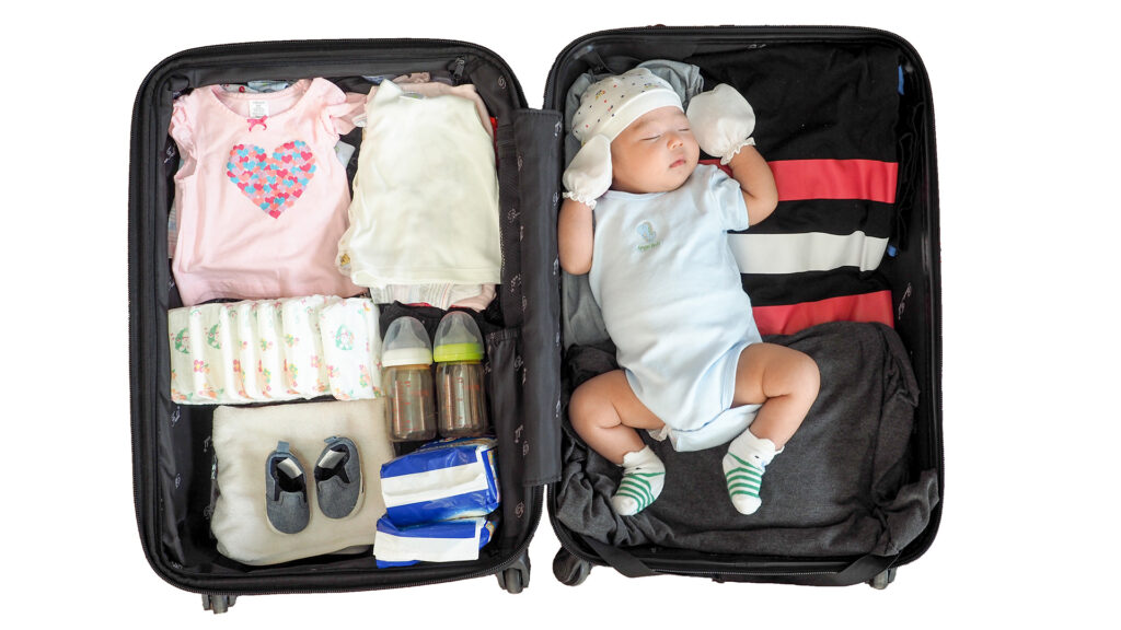 A newborn sleeping inside a suitcase surrounded by essential items like diapers and baby bottles for flying with a newborn.
