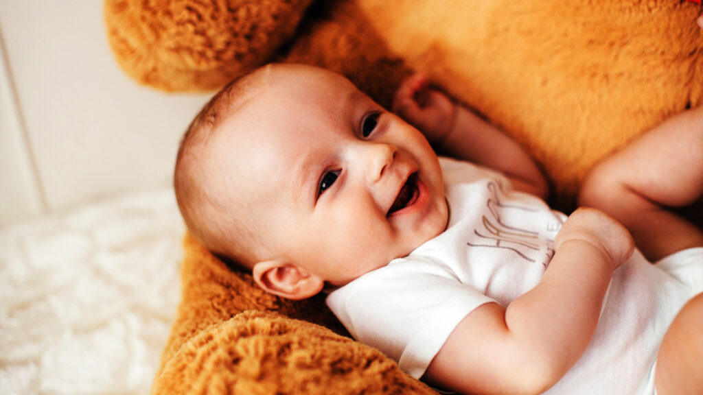 A smiling baby resting on a soft teddy bear, happy and calm during the flight. Flying with a newborn can also be a joyful experience.