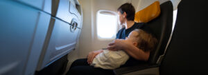 A parent holding a newborn while flying, gazing out the airplane window. Flying with a newborn requires patience and preparation.