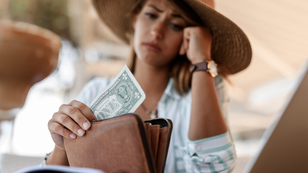 A closeup of a worried woman holding a single dollar bill in her wallet, possibly concerned about her expenses after deciding to book a hotel.