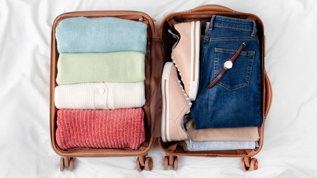 A neatly packed suitcase with cozy sweaters, shoes, and a watch, showcasing a well-thought-out winter packing list.