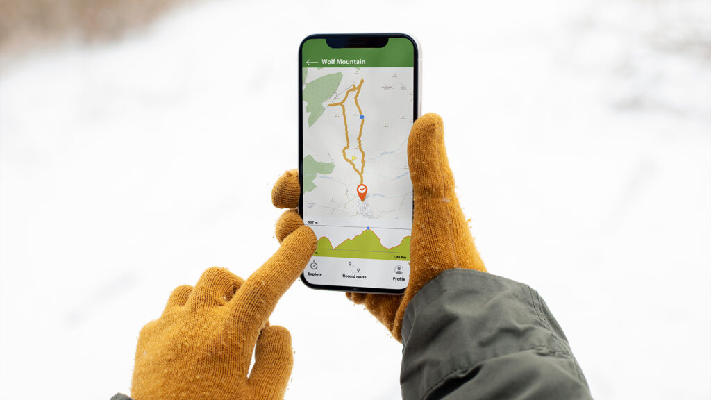 A person checking a winter map on their phone while on a snowy mountain route, ensuring proper winter driving directions.