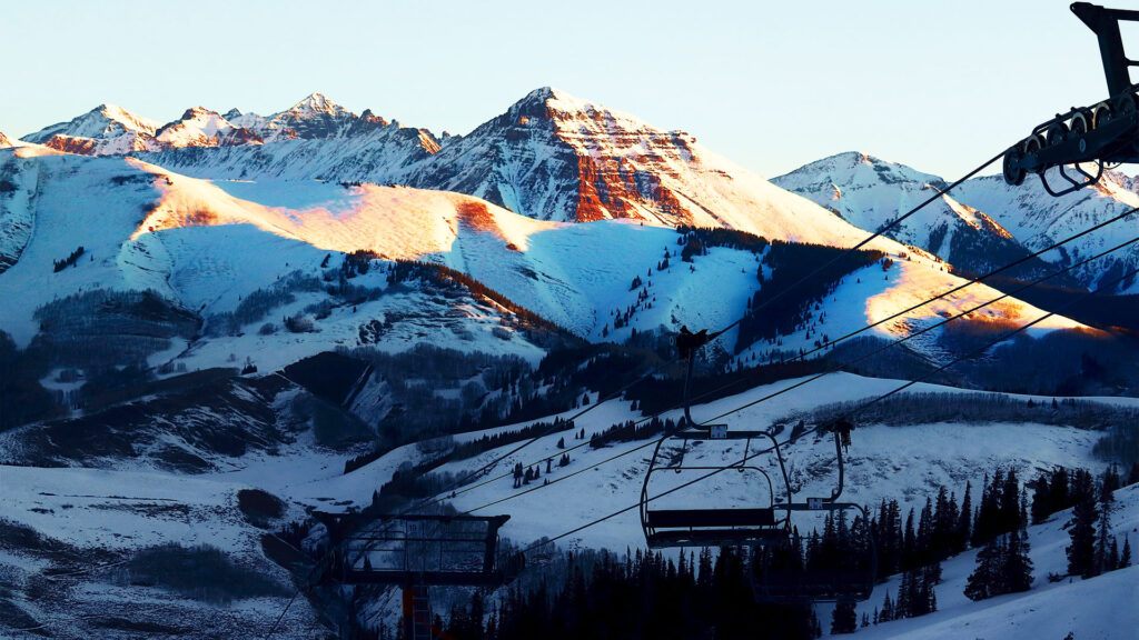 A serene view of a Crested Butte Colorado ski town’s chairlift carrying skiers up the mountain with beautiful snow-covered slopes.