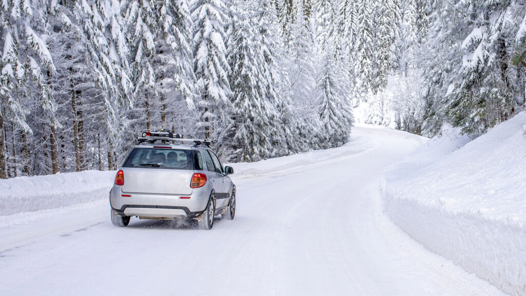 A car driving on a winding snow-covered road through a forest, highlighting the challenges of winter driving conditions.