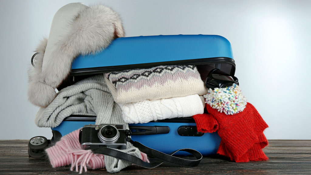 A suitcase packed with winter gear, including sweaters, hats, and a camera, for a trip to Alaska in December.