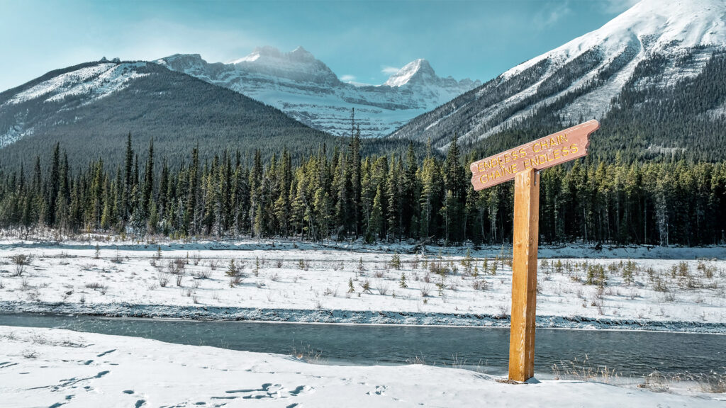 Snow-covered mountains in Alaska with a wooden trail sign for the "Endless Chain" path.