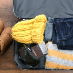 A suitcase filled with cozy winter essentials like boots, a warm yellow knit hat, a scarf, and a sweater, perfect for a winter getaway.