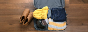 A suitcase filled with cozy winter essentials like boots, a warm yellow knit hat, a scarf, and a sweater, perfect for a winter getaway.
