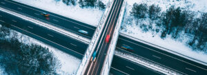 Aerial view of a snow-covered highway, showcasing a winter driving route with cars passing through the snowy landscape.