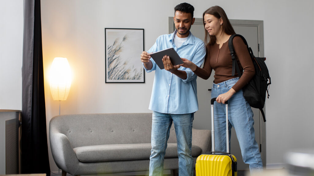 A couple reviewing hotel booking options on a tablet while preparing for travel.