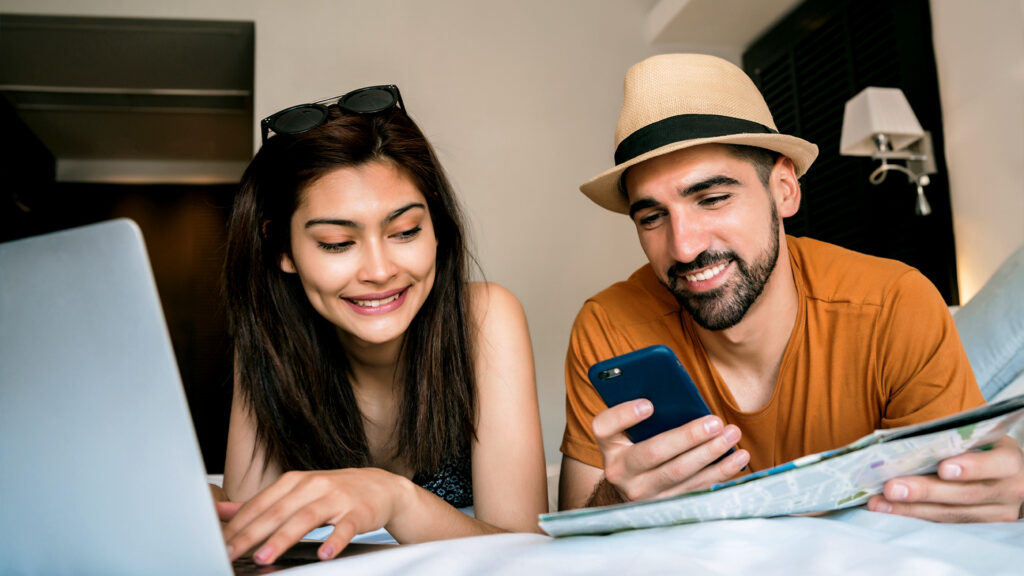A couple planning their February getaway, smiling as they research destinations on their devices in a hotel room.
