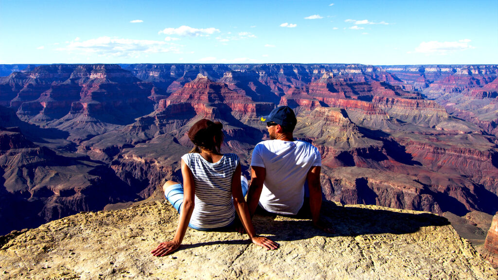 A couple sitting on the edge of the Grand Canyon, with expansive desert landscapes.