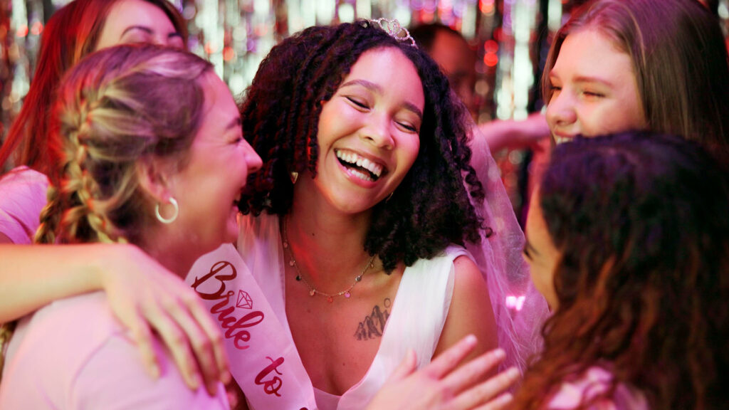 A bride-to-be laughing and enjoying time with friends at a bachelorette party in a vibrant setting, filled with joy and celebration.