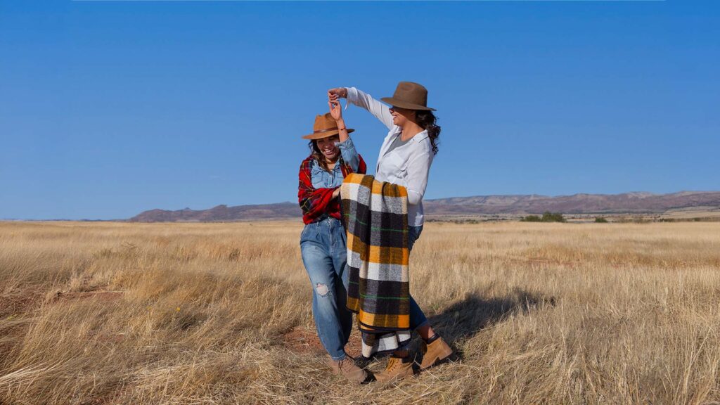 Two women dancing and enjoying each other's company on an open Texan plain under a clear blue sky, embracing the spirit of adventure.