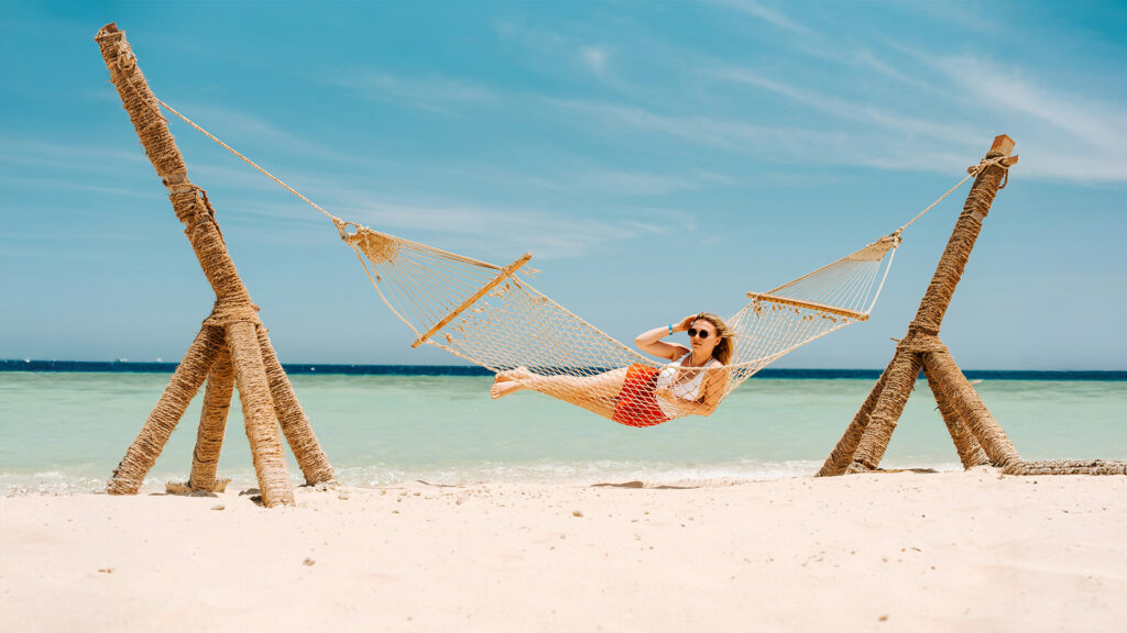 Relaxing hammock on a beautiful sandy beach with clear blue water and perfect skies.