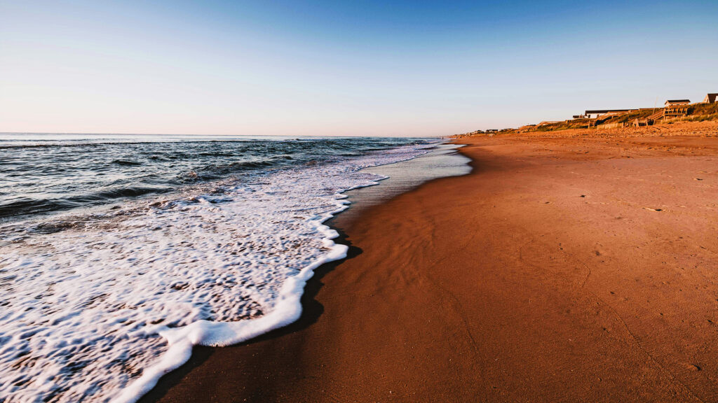 A peaceful beach at sunset, with gentle waves washing onto the shore and the soft glow of evening light illuminating the sandy beach.