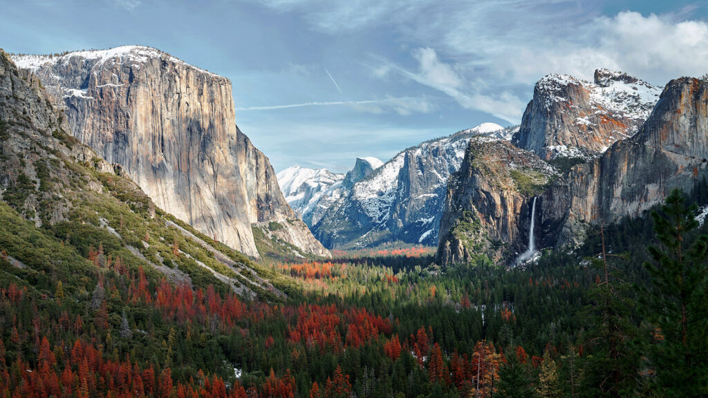 The iconic El Capitan in Yosemite National Park, featuring a snowy backdrop and vibrant red and green foliage.