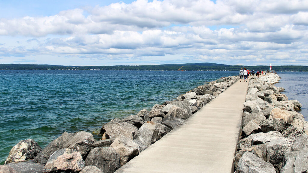 A scenic walkway along a jetty leading into a tranquil lake surrounded by lush green hills, perfect for an underrated summer getaway.