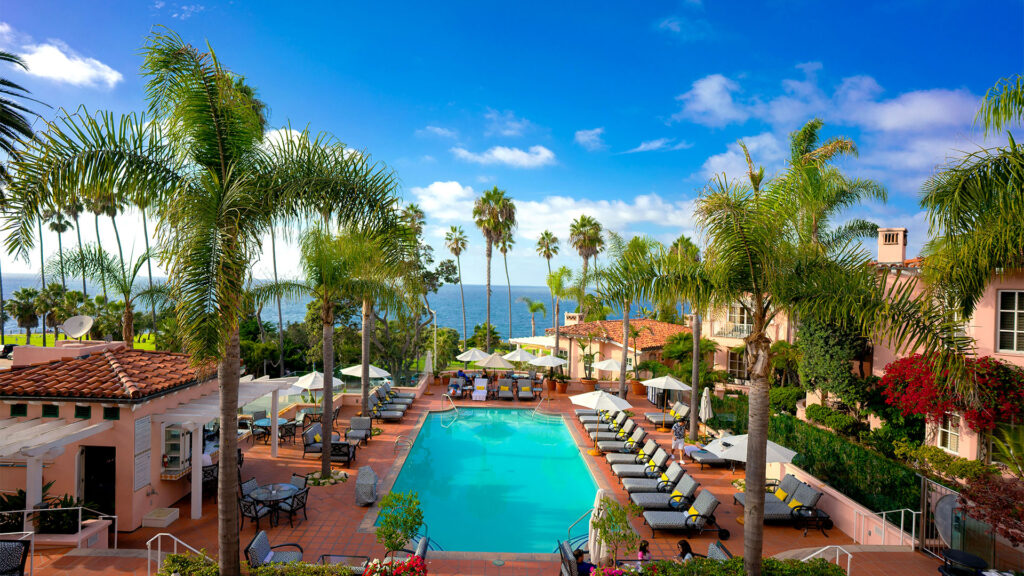 Poolside view with palm trees and sun loungers at a luxury resort with a scenic ocean view.